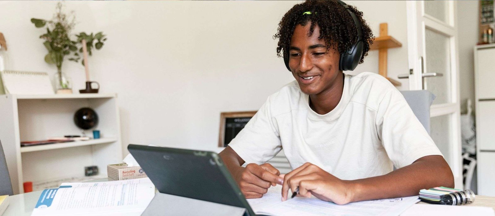 english1 Young man wearing headphones and smiling while studying on a tablet at home during online english classes for adults