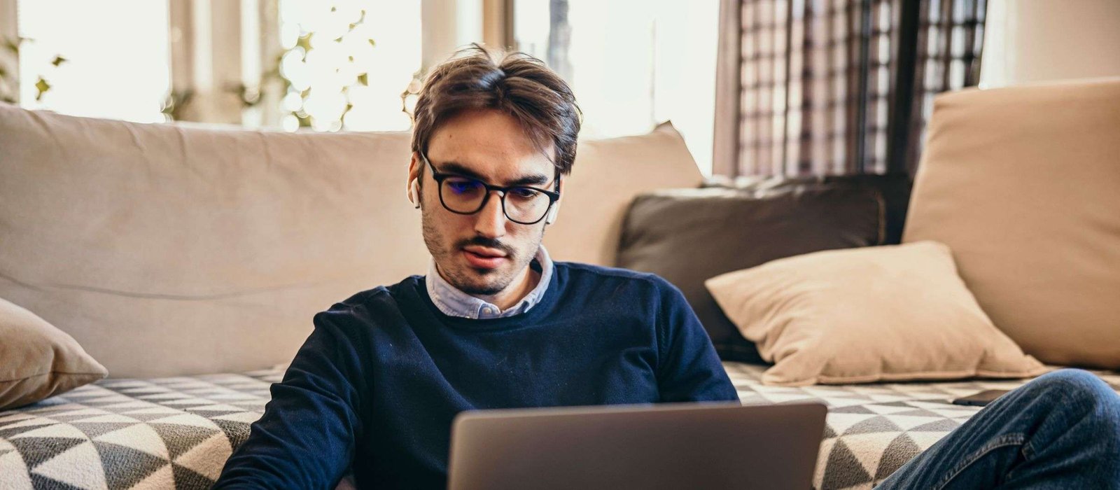 german Young man wearing earphones, studying and taking German language courses online while sitting comfortably on a sofa