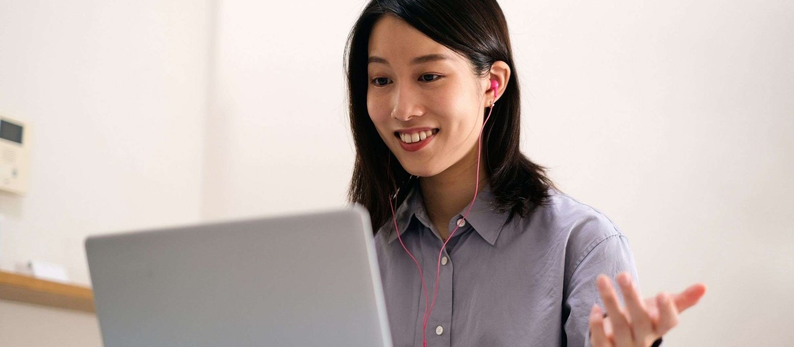 Smiling woman participating in Japanese language classes online, wearing pink headphones