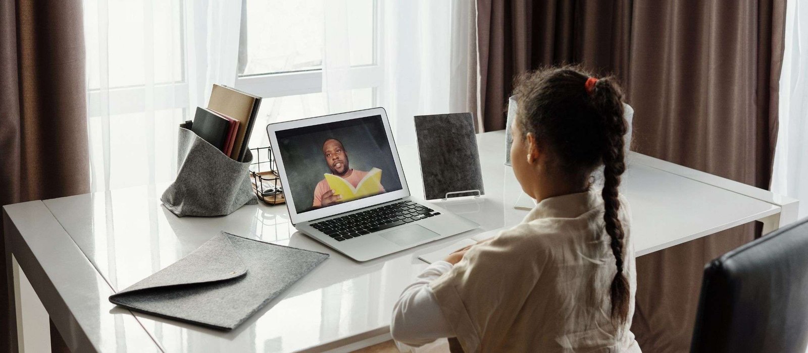Young girl attending online Arabic lessons, watching a teacher on a laptop screen while taking notes