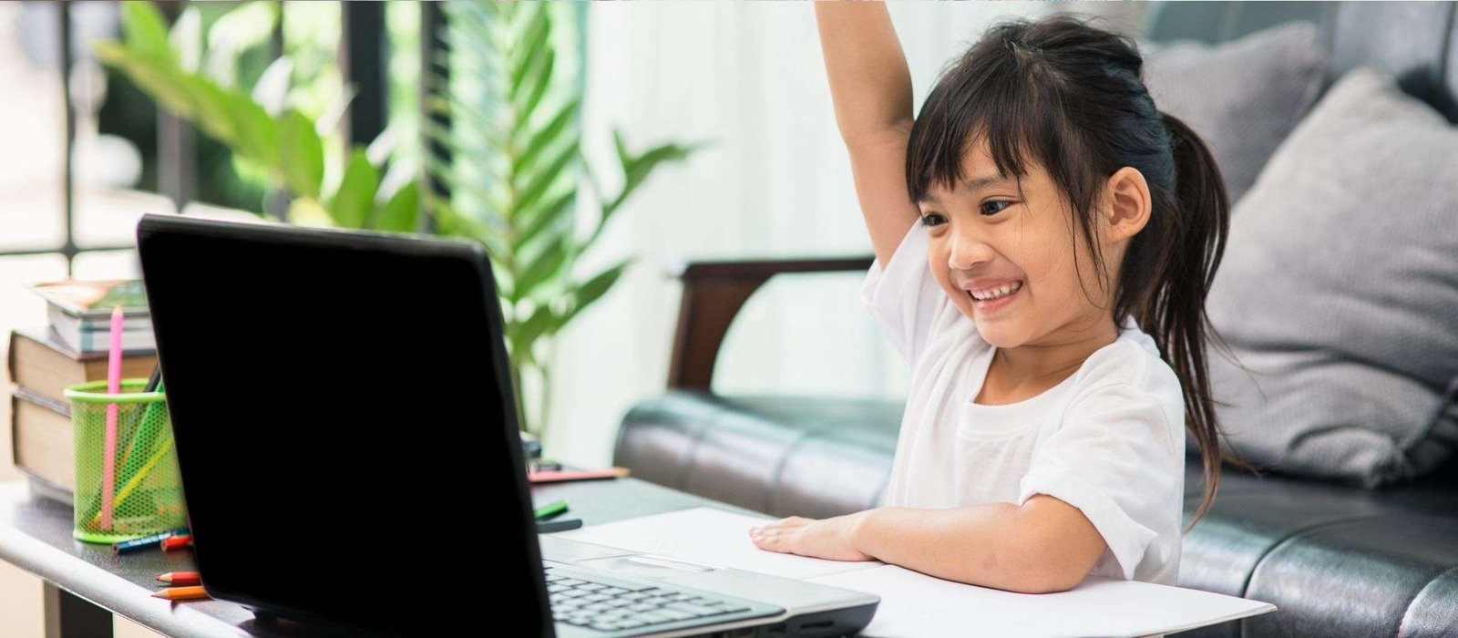 kids vietnam Young girl raising her hand while learning Vietnamese language online, sitting at a desk with a laptop