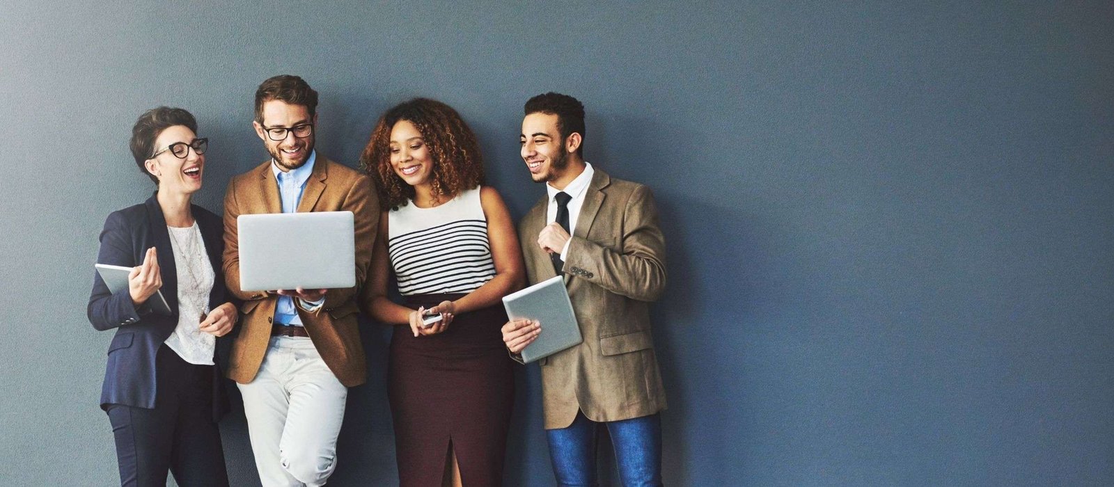 Four diverse professionals smiling and looking at a laptop together during a language learning online session against a modern office background