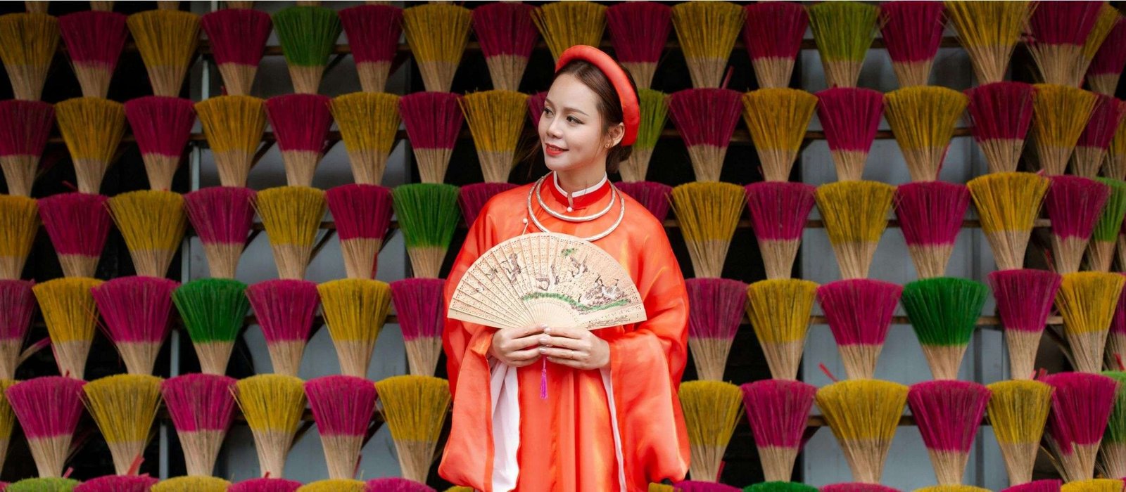 vietnamese Smiling woman in traditional Vietnamese attire, holding a fan while standing in front of vibrant incense sticks, symbolizing her engagement in learning the Vietnamese language