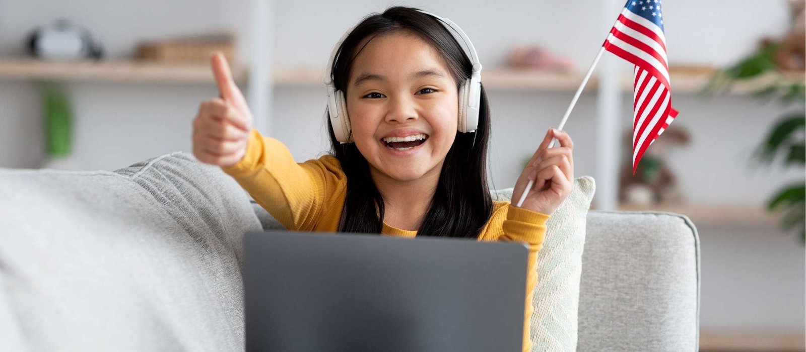 Young girl participating in English study online in Australia, smiling and holding a US flag while sitting with her laptop